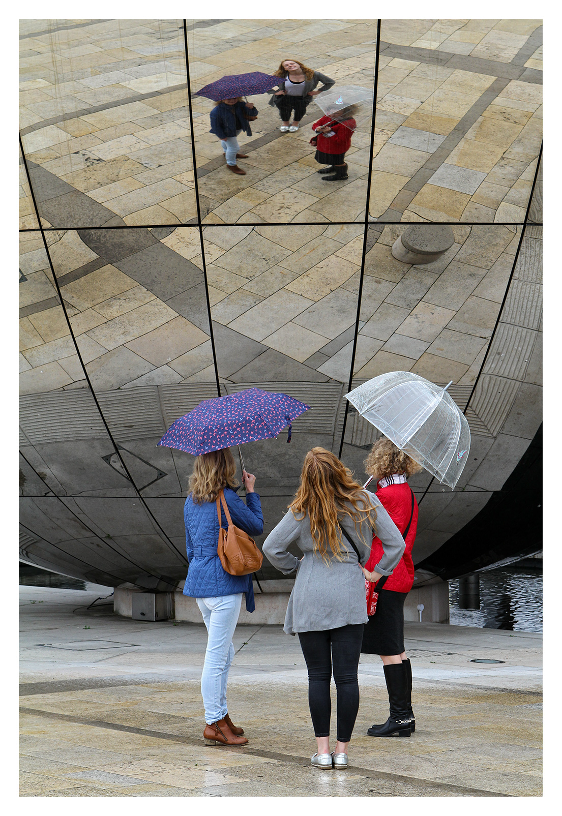 Three women looking at their reflection on the mirror globe, Millenium Square, Bristol, England