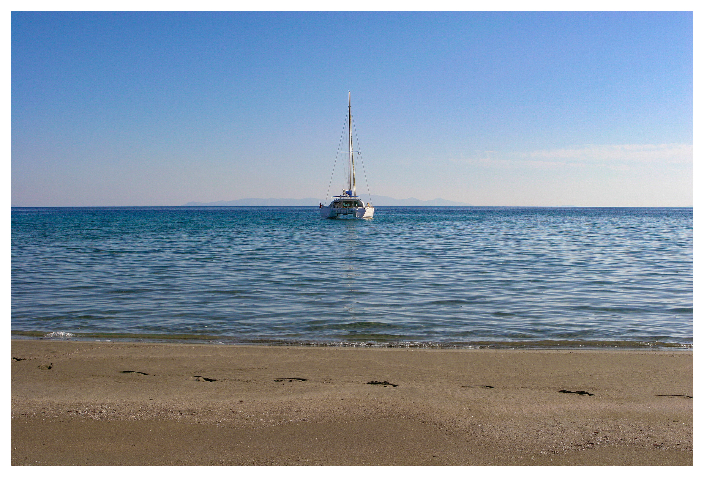 Yachting photography: A catamaran anchored off a desserted beach in Paros. Blue sky and a blue sea, Cyclades, Greece